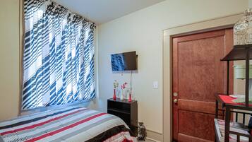 A bedroom with a bed, a TV on the wall, a door, and a window with curtains.