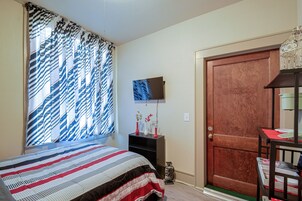 Un dormitorio con cama, televisor en la pared, una puerta y ventana con cortinas.