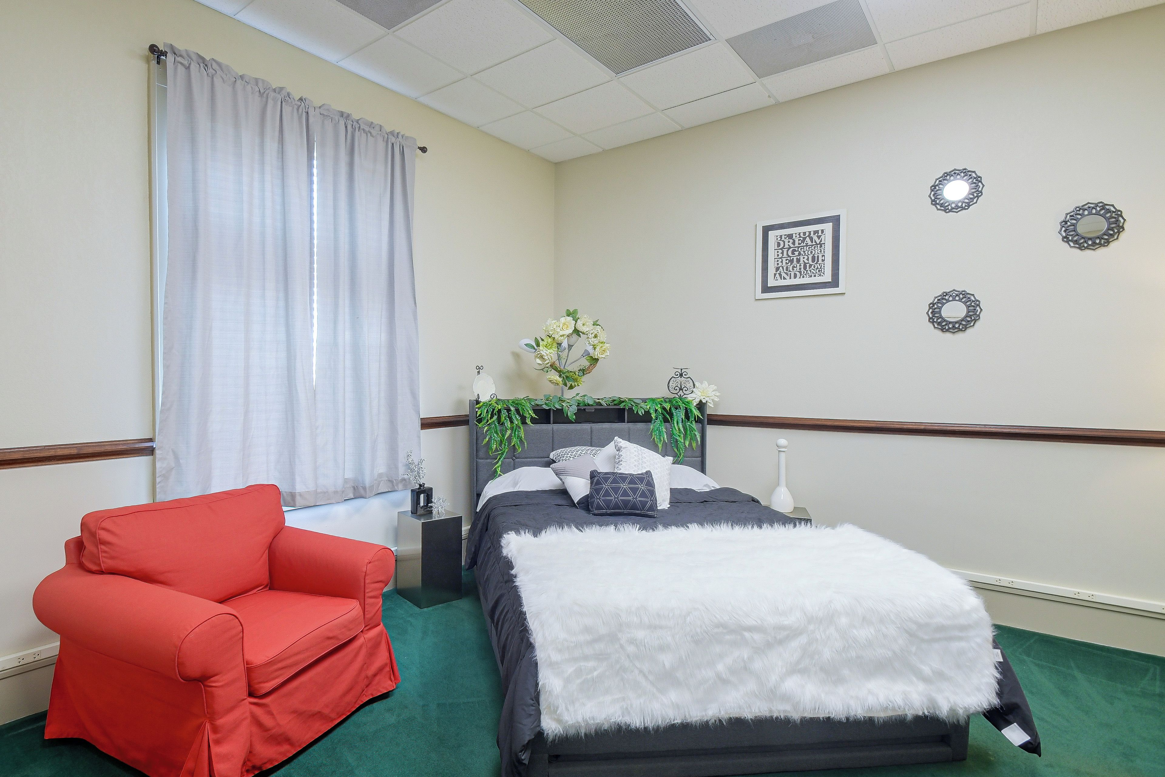 A hotel room with a bed, a red armchair, a nightstand, and decorative wall mirrors.