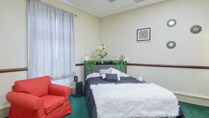 Una habitación de hotel con una cama, un sillón rojo, una mesita de noche y espejos decorativos en la pared.