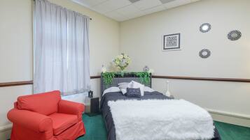 A hotel room with a bed, a red armchair, a nightstand, and decorative wall mirrors.