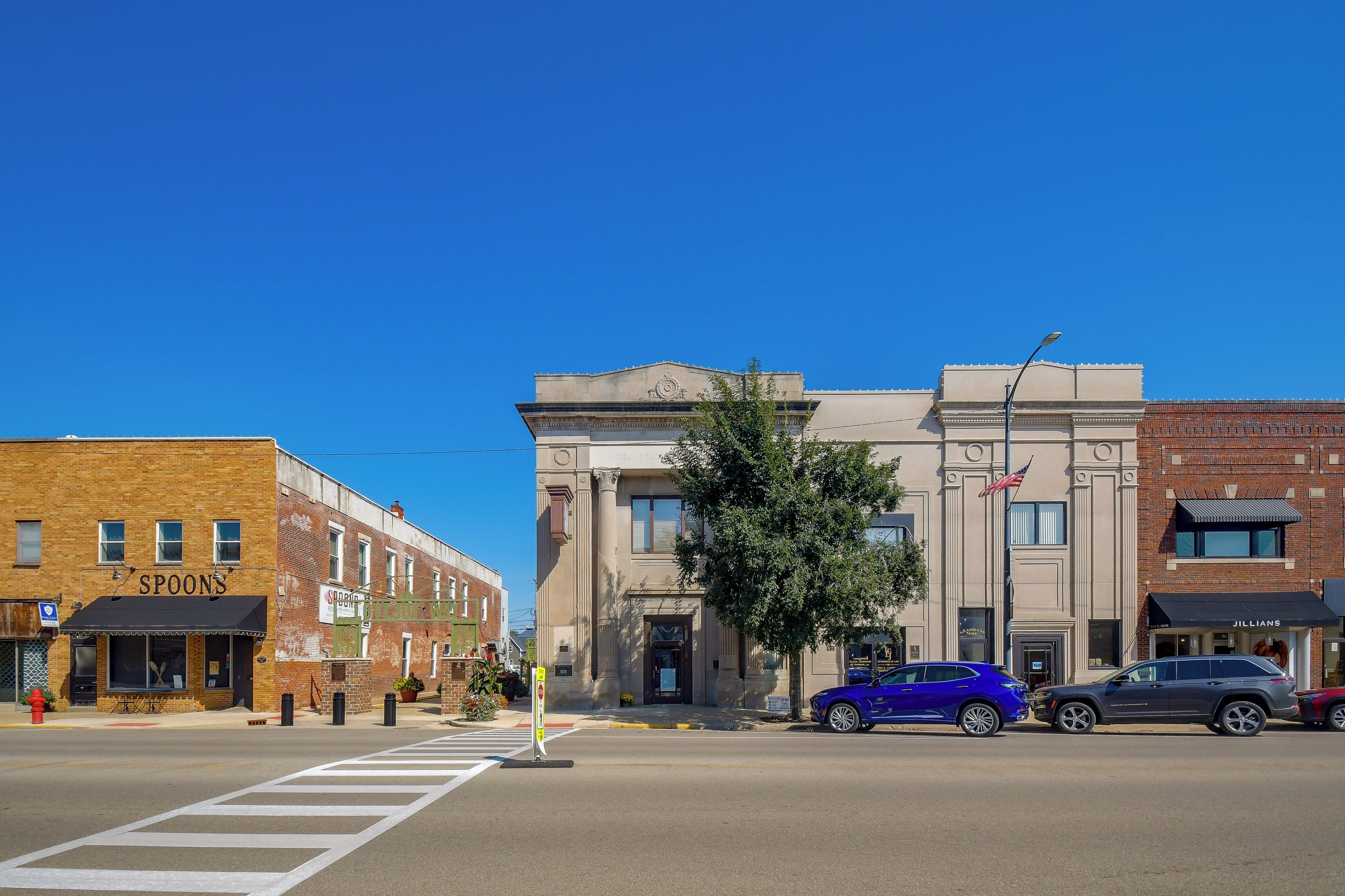 A street view with a building featuring a large entrance, a crosswalk, and parked cars.