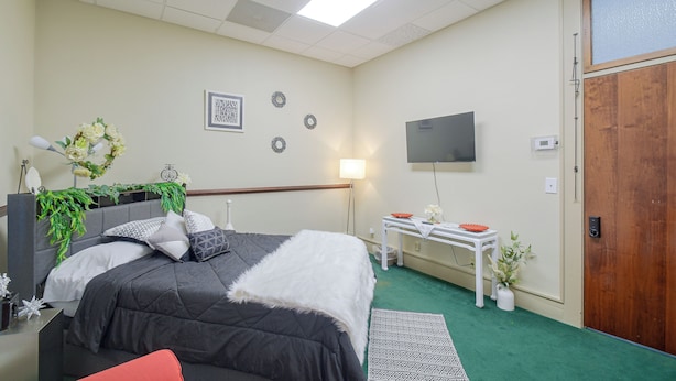 A bedroom with a bed, bedside table, TV, and a wooden door. - Walkable Main Street Apartment in Princeton! (Princeton)