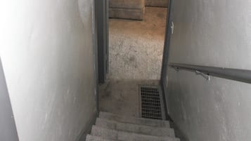 Uma escada estreita com corrimão de metal, degraus revestidos de carpete e grade metálica na base.