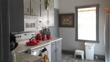 A kitchen with a microwave, stove, and red kettle. There is a window with a view of the outside.