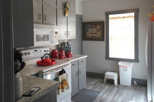 A kitchen with a microwave, stove, and red kettle. There is a window with a view of the outside.