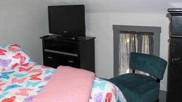 A hotel room with a bed, a chair, a TV on a stand, and a window with curtains.