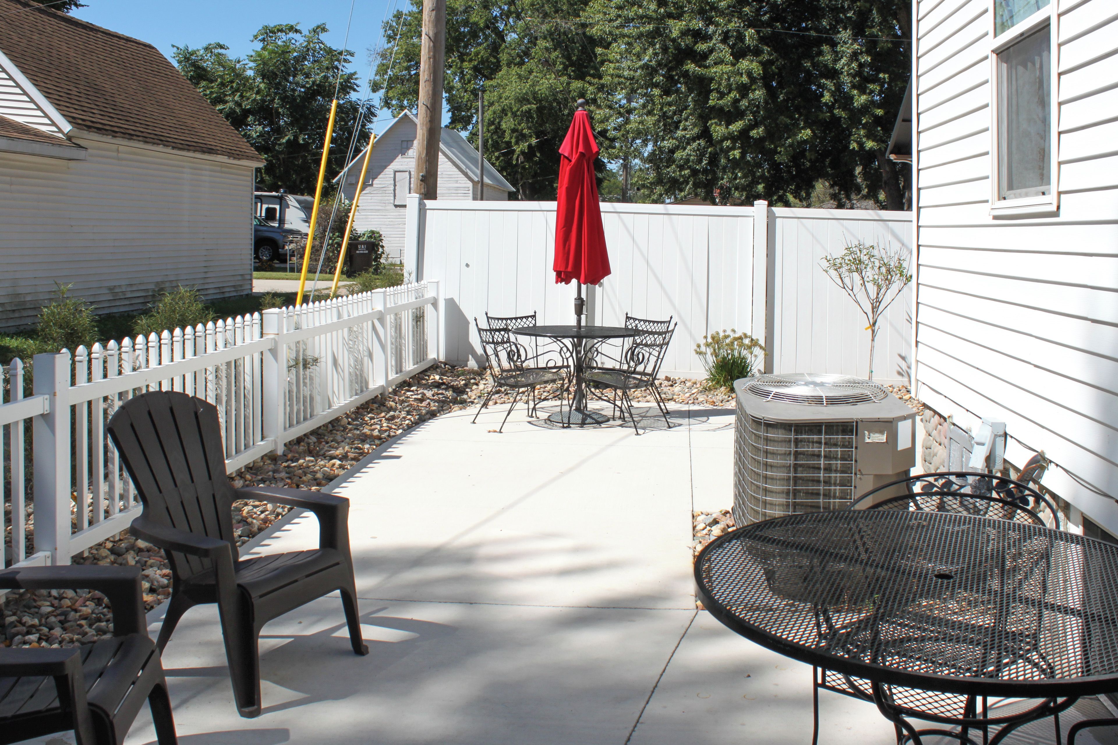 A patio with a table and chairs, a red umbrella, and an air conditioning unit.