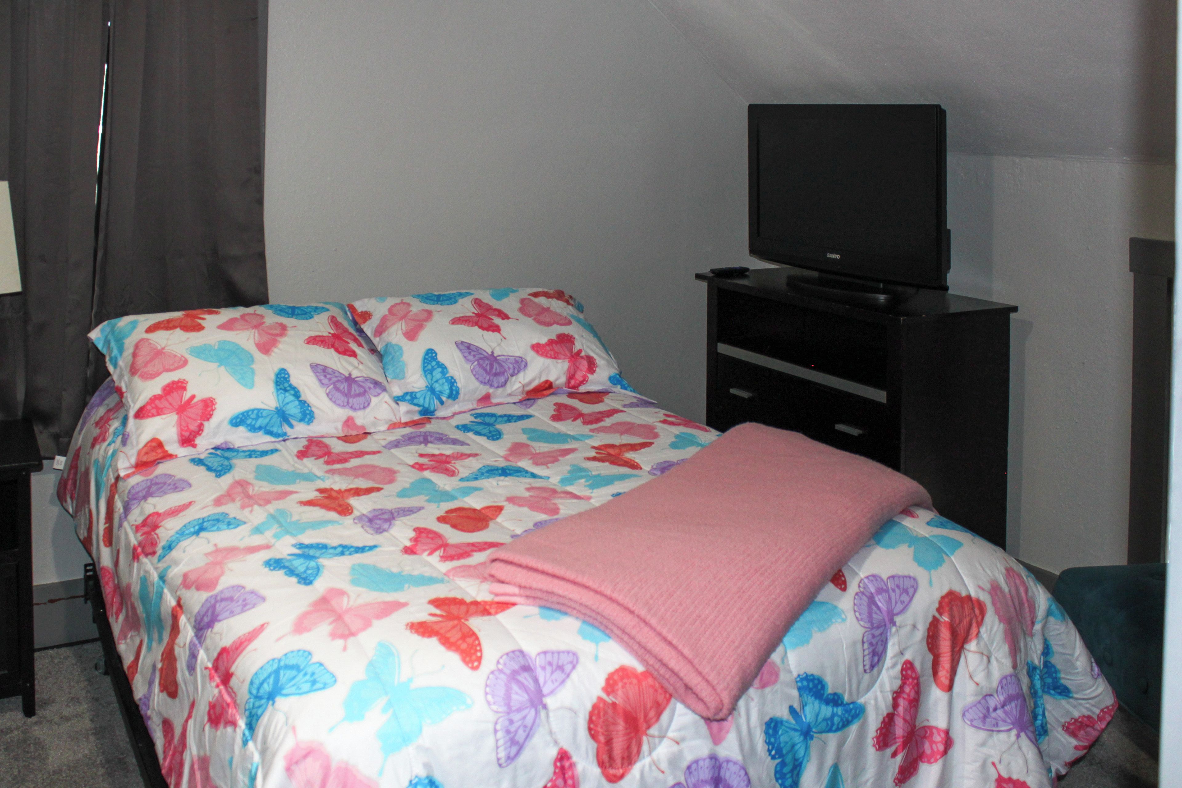 A bedroom with a bed, a television on a stand, and a dresser.