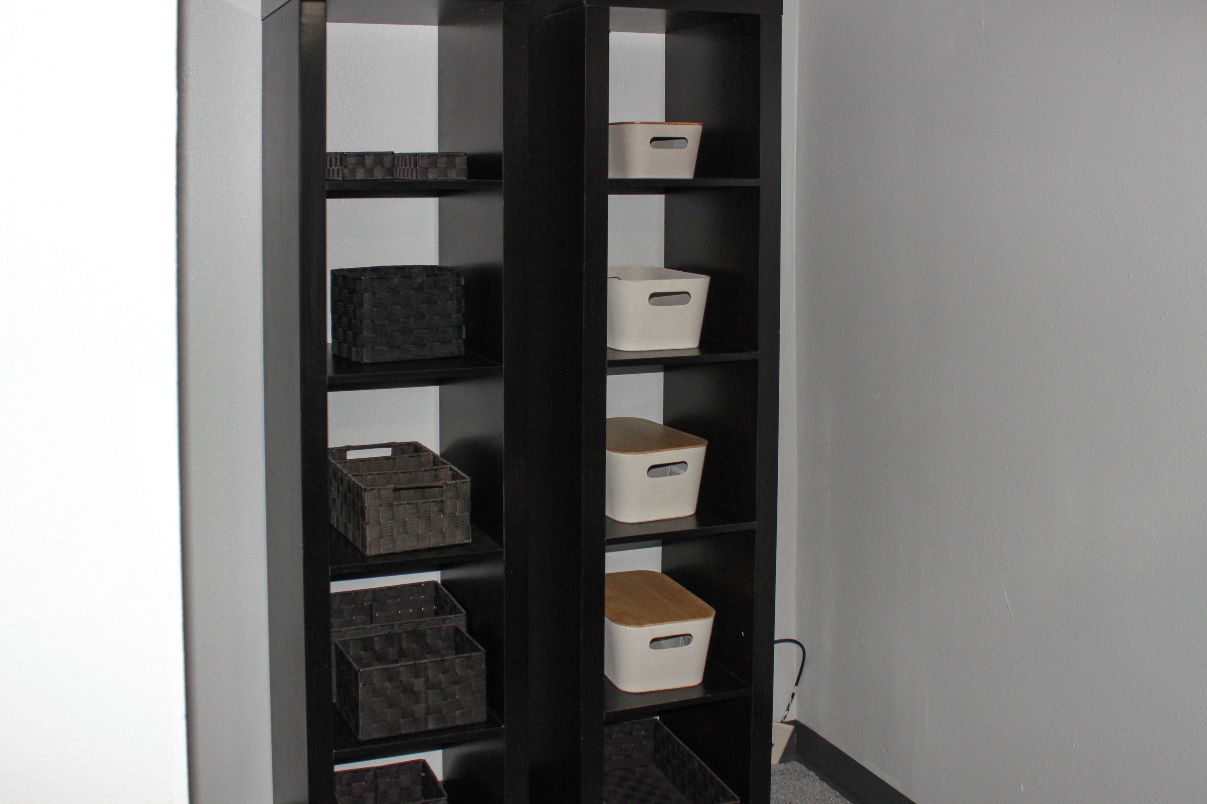 A black shelving unit with multiple storage bins against a wall.