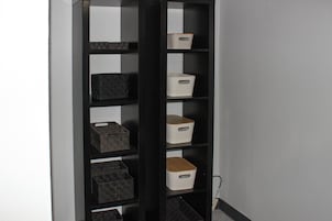 A black shelving unit with multiple storage bins against a wall.