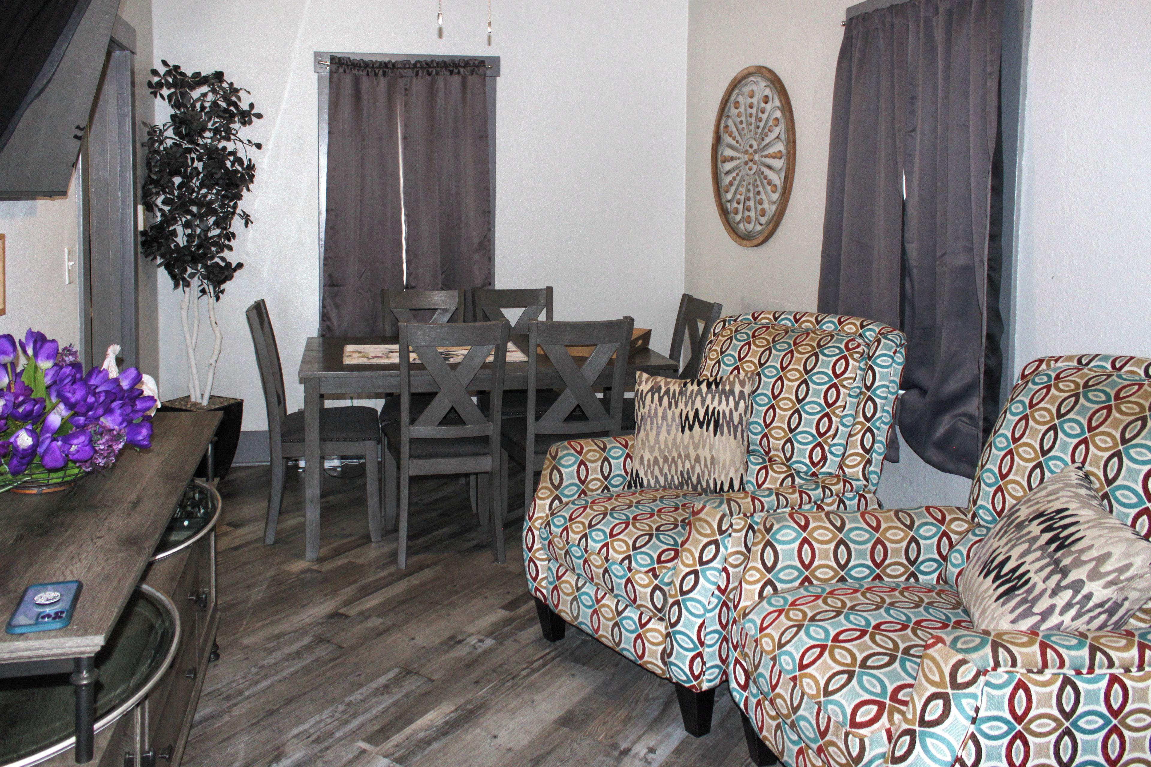 A compact living space with a dining table, chairs, a sofa, and a decorative wall piece.