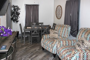 A compact living space with a dining table, chairs, a sofa, and a decorative wall piece.