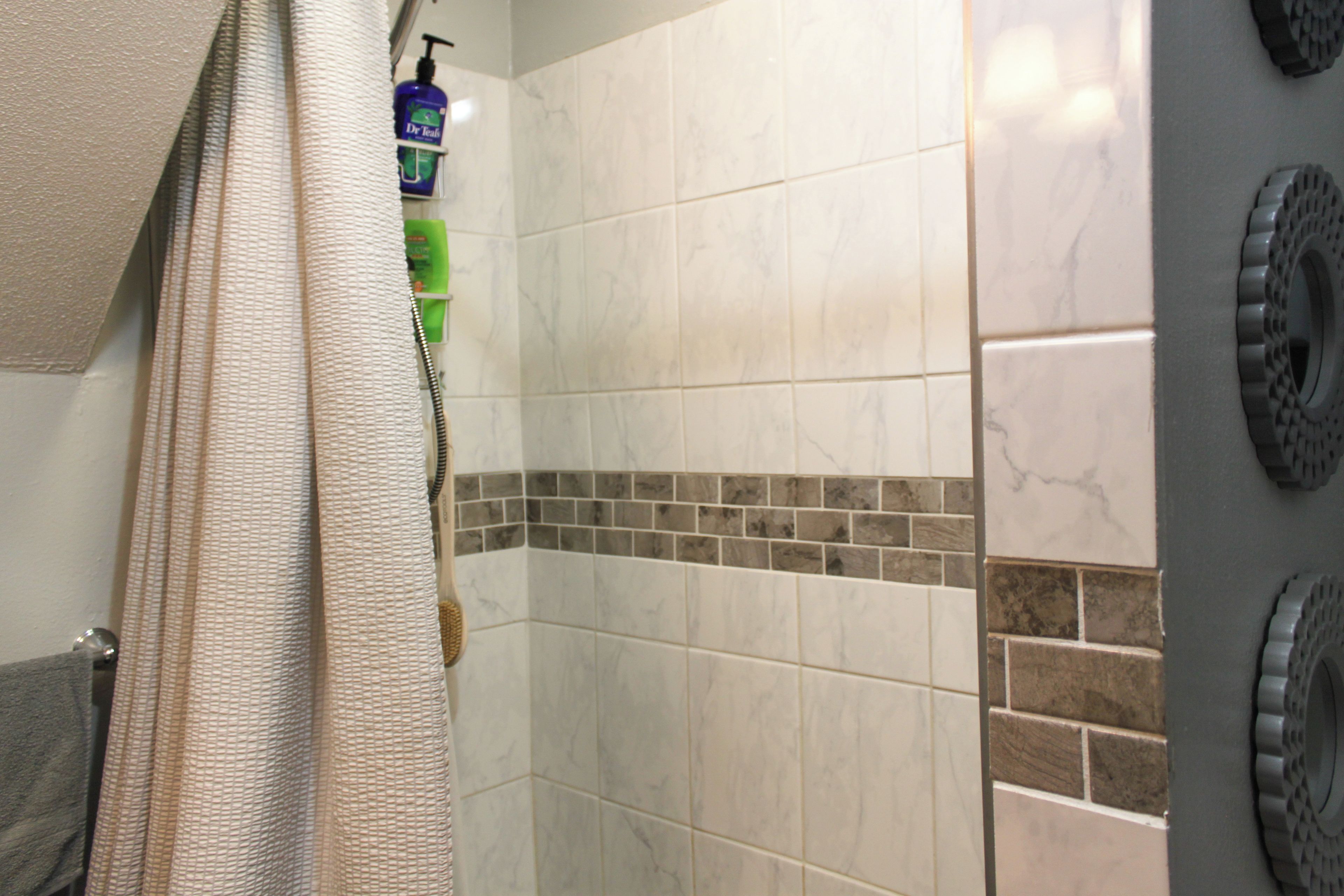 A bathroom with a shower, tiled walls, a towel rack, and toiletries.