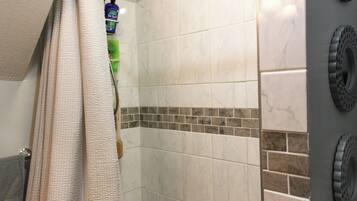 A bathroom with a shower, tiled walls, a towel rack, and toiletries.