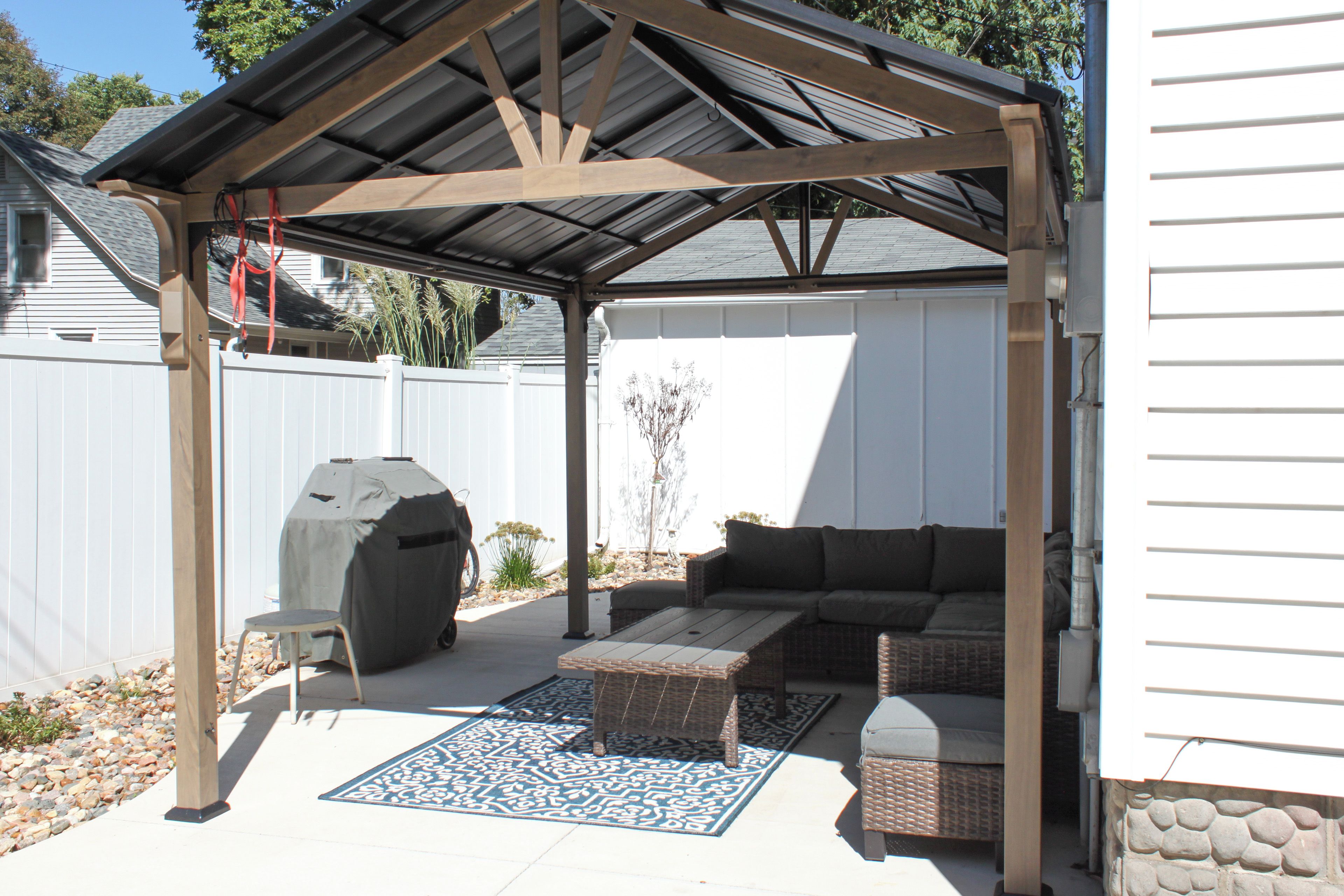 A covered patio area with a grill, seating, and a decorative rug.