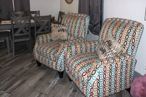 A room with a patterned armchair, a wooden dining table with chairs, and a patterned rug.