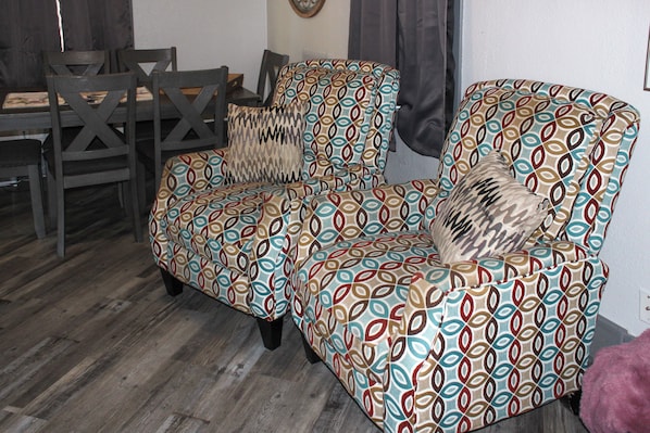 Une pièce comprenant un fauteuil à motifs, une table à manger en bois avec des chaises, et un tapis à motifs.