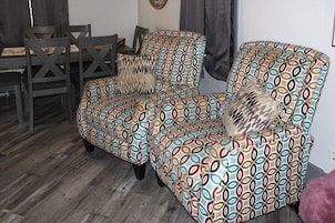 Una habitación con un sillón estampado, una mesa de comedor de madera con sillas y un tapete con diseño.