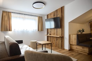 A modern living room with a flat-screen TV mounted on a wooden wall, a sofa, a small table, and a staircase leading to an upper level. - Modern Suite With Outdoor Sauna (Gaschurn)