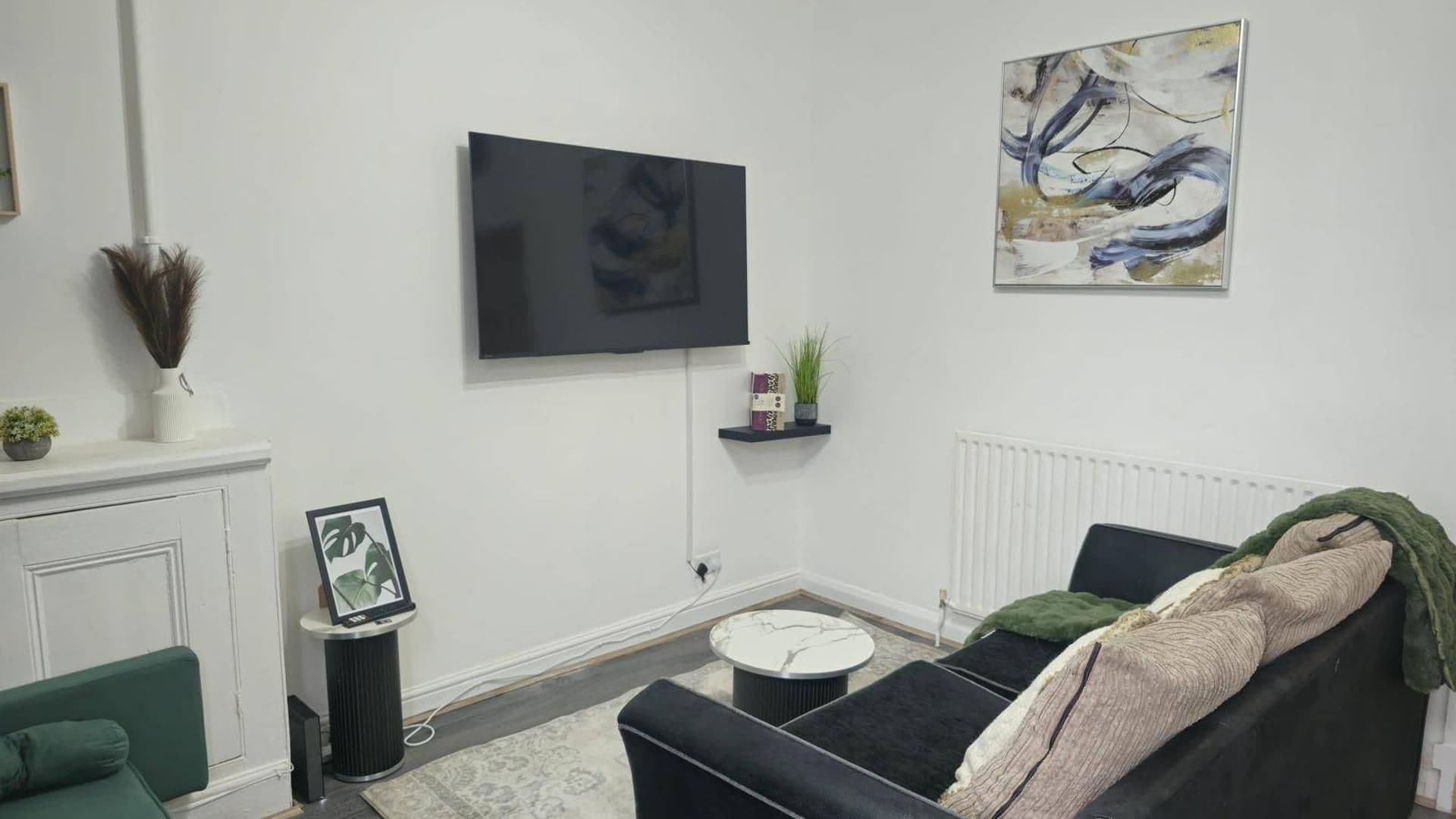 A living room with a flat-screen TV mounted on the wall, a sofa, a small round coffee table, and a fireplace.