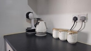 Una encimera de cocina con una cafetera, un hervidor y tres tarros con tapa.