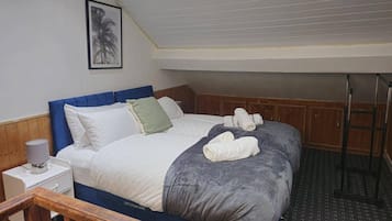 A bedroom with a bed, pillows, a bedside lamp, a towel, and a framed picture on the wall.