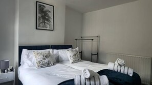 Una habitación de hotel con una cama, una mesita de noche, un radiador y un cuadro enmarcado en la pared.