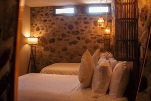 Ein Zimmer mit Stehwänden, zwei Betten mit weißen Laken, einer Stehlampe und einer Lampenkonstruktion aus Bambus.