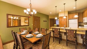 A dining area with a wooden table set for four, surrounded by chairs, and a kitchen area with wooden cabinets and a refrigerator. - 2-bedroom resort in superb Gatlinburg with fitness room, jetted bath tubs, w/AC (Gatlinburg)
