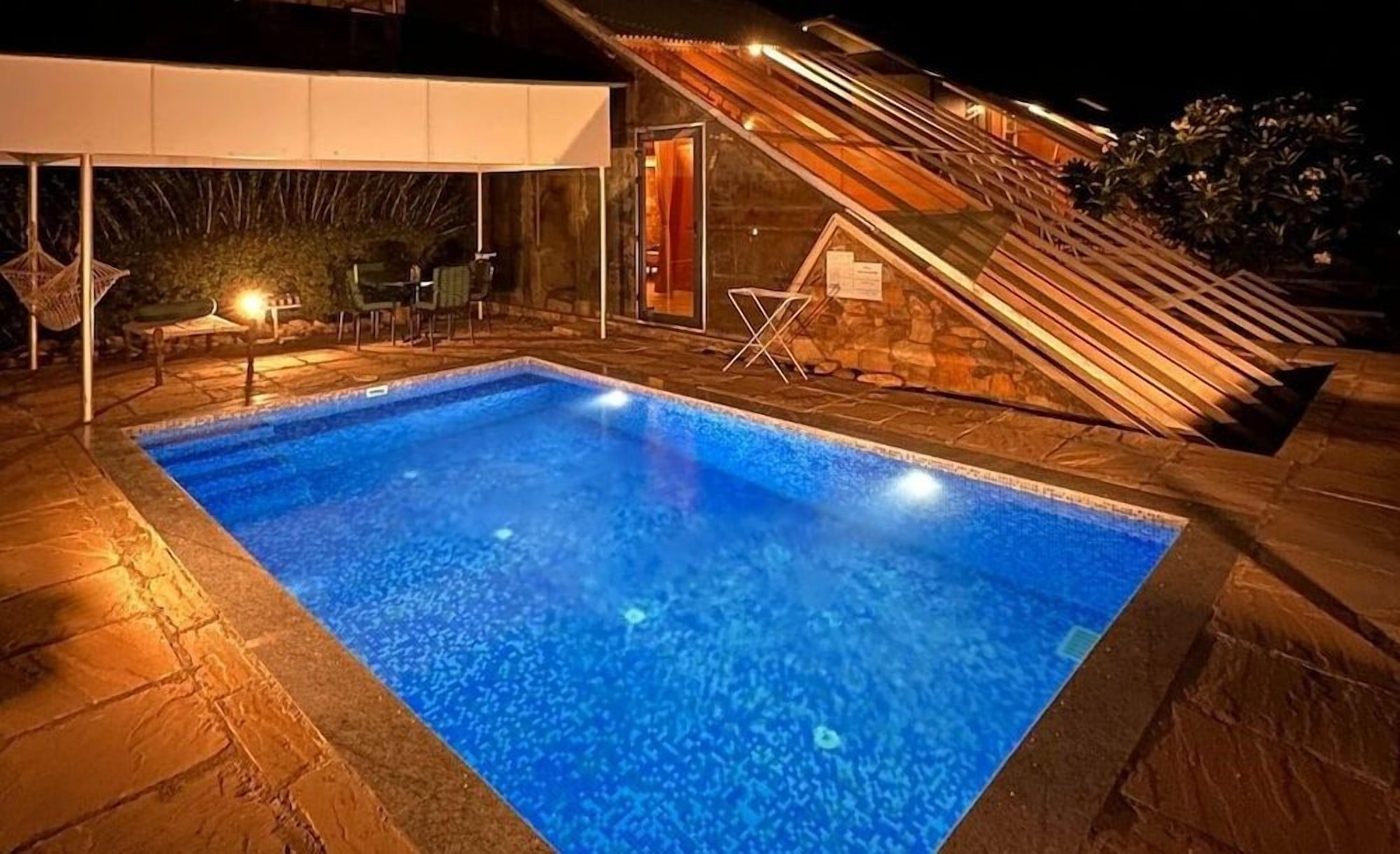 A swimming pool with a stone deck, a covered seating area, and a staircase leading to an upper level.