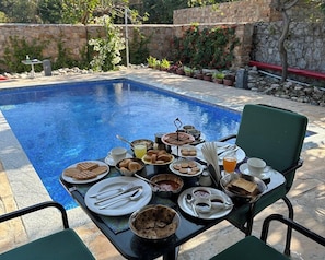 A dining table set for breakfast by a pool with various dishes and drinks. - Mana Hotel Ranakpur (Desuri)