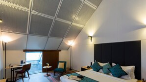 A modern hotel room with a large bed, a desk, a chair, and a view of the outdoors. - Mana Hotel Ranakpur (Desuri)