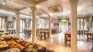 A spacious dining area with multiple tables and chairs, a buffet with various food items, and a view through the windows. - Rawla Narlai Luxury Heritage Hotel (Desuri)