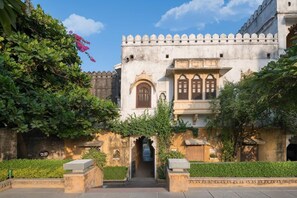 A traditional building with a central arched entrance, surrounded by greenery and a clear sky.