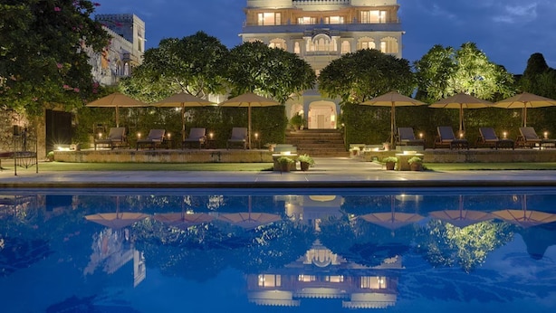 A large, illuminated building with a reflective pool in front, surrounded by lounge chairs and umbrellas. - Rawla Narlai Luxury Heritage Hotel (Desuri)