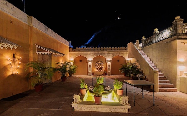 A courtyard with a fountain, potted plants, and a staircase leading to an upper level.