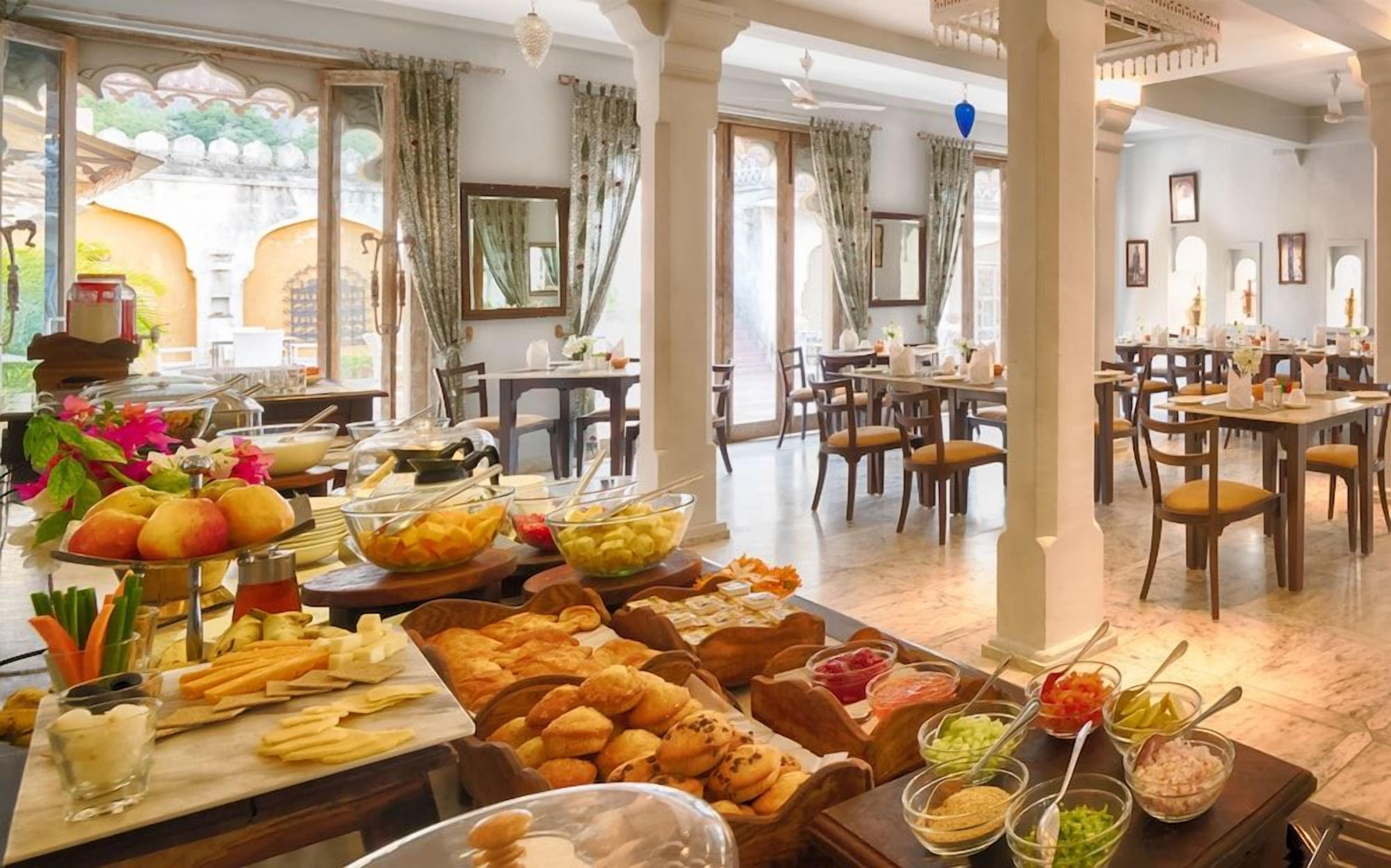 A dining area with multiple tables, a buffet with various food items, and a view of the outside through large windows.