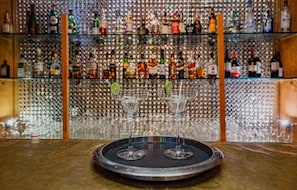 A bar area with a glass shelf filled with various bottles and a tray with two glasses. - Rawla Narlai Luxury Heritage Hotel (Desuri)