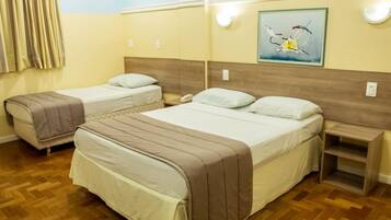 A hotel room with two beds, wooden flooring, a painting on the wall, and a nightstand with a lamp.