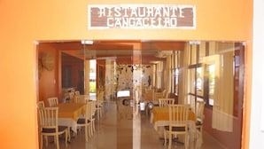 A restaurant with a mirrored entrance, wooden tables, and chairs. - Hotel Grande Rio (Petrolina)