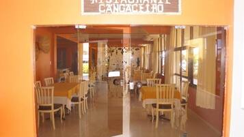 Restaurante com entrada espelhada, mesas e cadeiras de madeira.