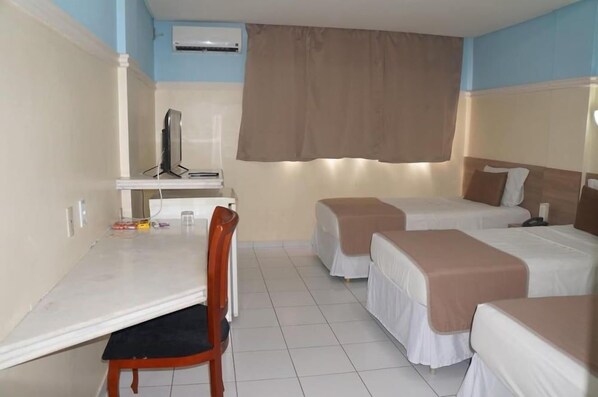 A hotel room with a desk, two beds, a chair, and a television.