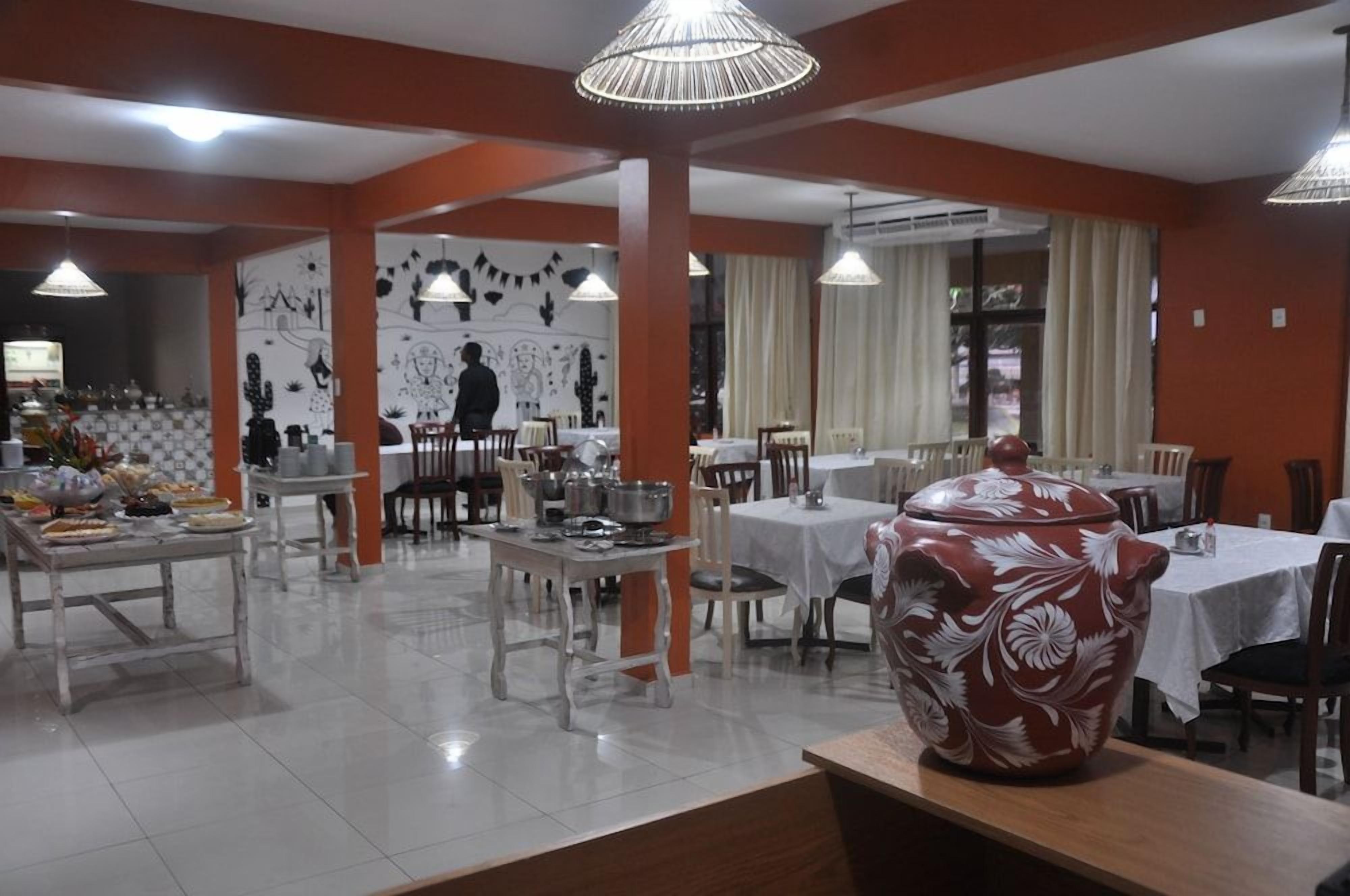A dining area with tables and chairs, a large decorative pot, and wall art.