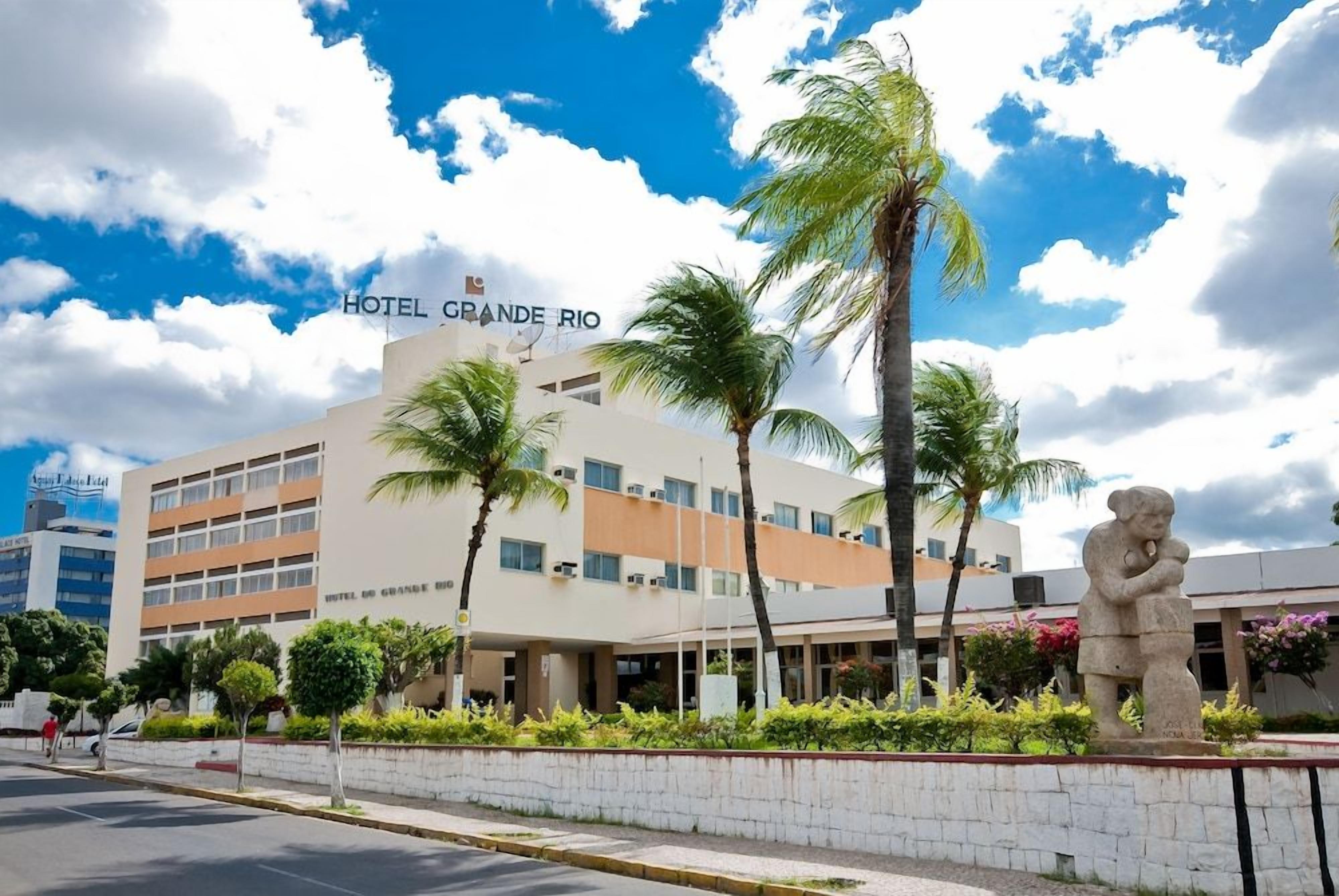A hotel with a sign reading 'HOTEL GRANDE RIO' and a statue of a man holding a child in front of it.