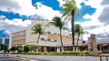 A hotel with a sign reading 'HOTEL GRANDE RIO' and a statue of a man holding a child in front of it.