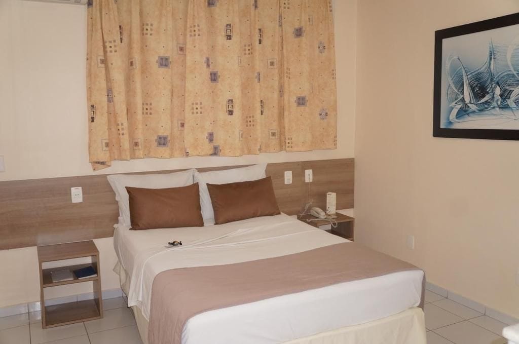 A hotel room with a bed, a nightstand, a telephone, and a painting on the wall.