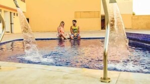 A pool with two people sitting on the edge, surrounded by a yellow building. - Hotel Grande Rio (Petrolina)
