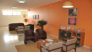 A living room with a sofa, chairs, a coffee table, a plant, and a bookshelf with magazines. - Hotel Grande Rio (Petrolina)
