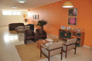 A living room with a sofa, chairs, a coffee table, a plant, and a bookshelf with magazines. - Hotel Grande Rio (Petrolina)